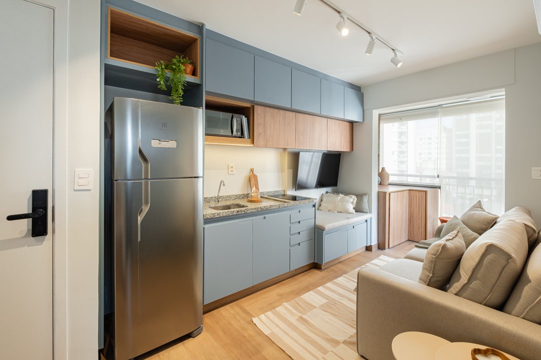 Studio Apto Cardeal com cozinha azul, sofá claro e marcenaria compacta.