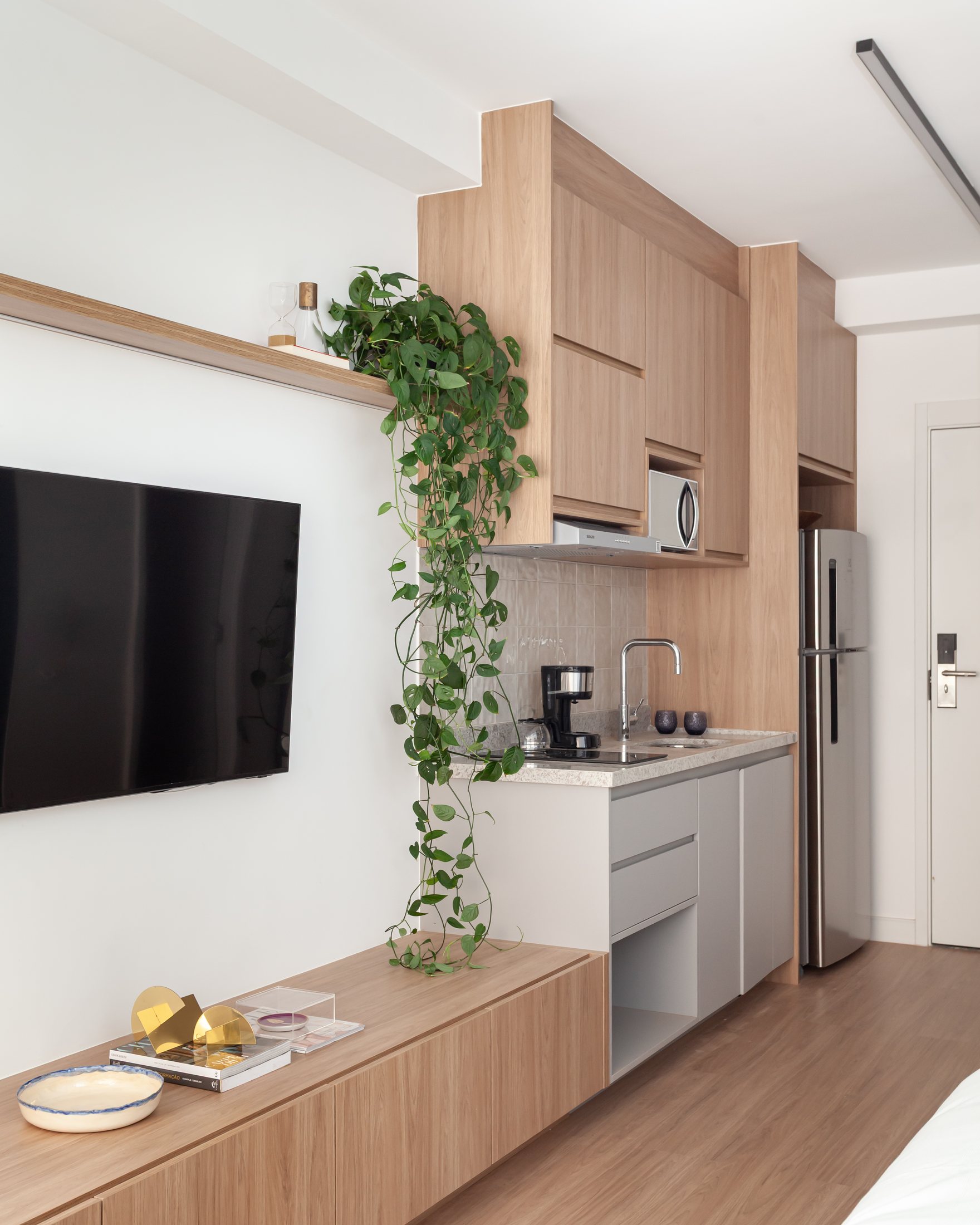 Studio Campo Belo com cama, painel de TV, cozinha compacta e planta pendente.